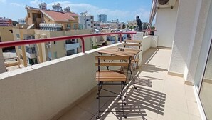 A balcony with a wooden table and chairs, a red railing, and a view of surrounding buildings. - Umm Haram whole apartment · 5 min walk to the Beach! NETFLIX & fast Internet (Larnaca)