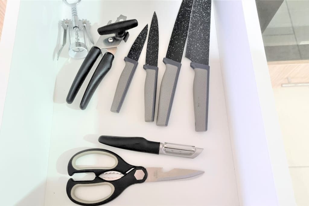 Eine Schublade mit verschiedenen Küchenutensilien, darunter Messer, eine Schere und ein Dosenöffner.