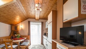 Una cocina compacta con televisión, armarios de madera y una zona de comedor con mesa y sillas.