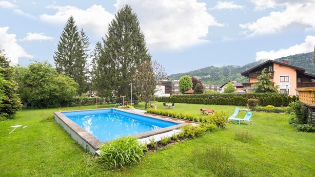 Una piscina rodeada de un césped cuidado, con algunas sillas de descanso y un pabellón.