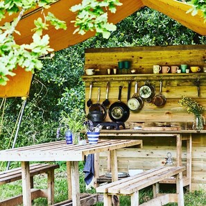 Una cucina esterna rustica con pareti in legno, pentole appese e un tavolo con panche.