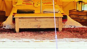 A tent with a bed inside, a wooden bench, a lantern, and a patterned rug.
