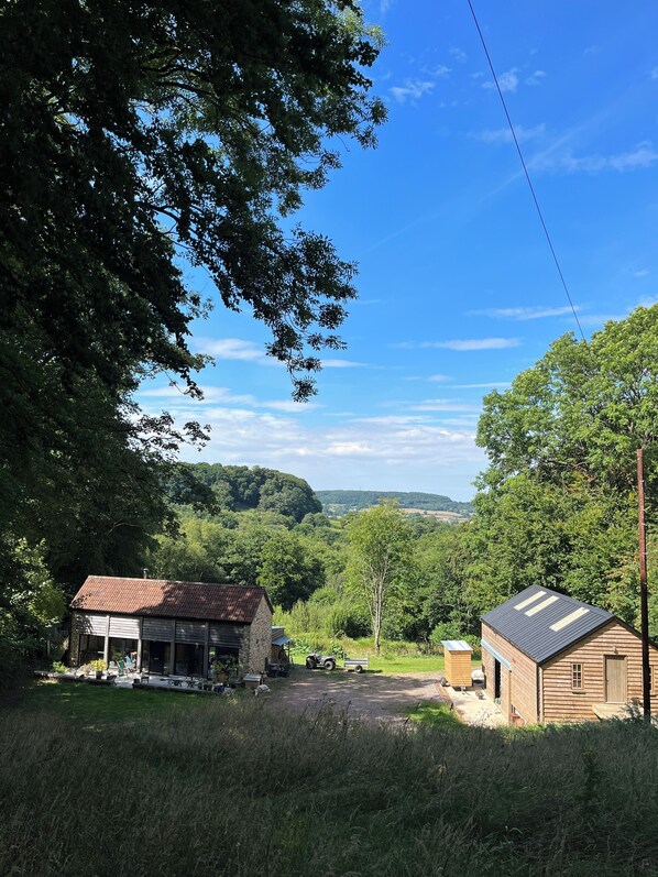 A rural setting with a small wooden building, a covered structure with a red roof, and a dirt road leading through a green landscape.