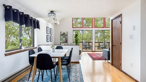 A dining area with a table and chairs, large windows, and a view of the outdoors. - Forest 2BR chalet w/ hot tub & backyard (Gerrardstown)