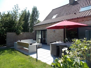 Relax on the patio with a comfortable sofa and dining table for two, surrounded by lush greenery.