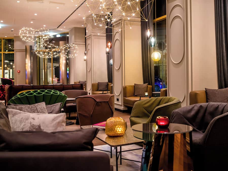 Un moderno vestíbulo de hotel con mobiliario contemporáneo, iluminación ambiental y ventanas amplias.