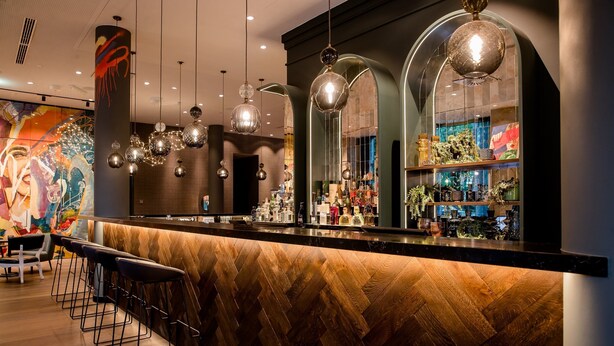 Eine Bar mit Holz-Fischgrätparkett, Barhocker und Pendelleuchten.