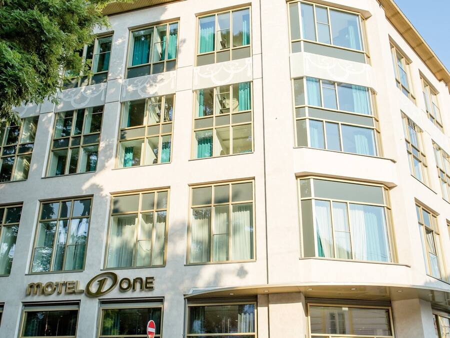 A multi-story building with a prominent 'Motel One' sign, large windows, and a corner entrance.