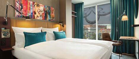 A hotel room with a large bed, a desk, a chair, a window with curtains, and a painting on the wall.