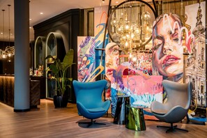 A modern interior with two blue chairs, a large abstract painting, and a chandelier. - Motel One Graz (Graz)