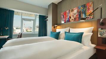 A hotel room with a large bed, a desk, and a view of the cityscape through the window.