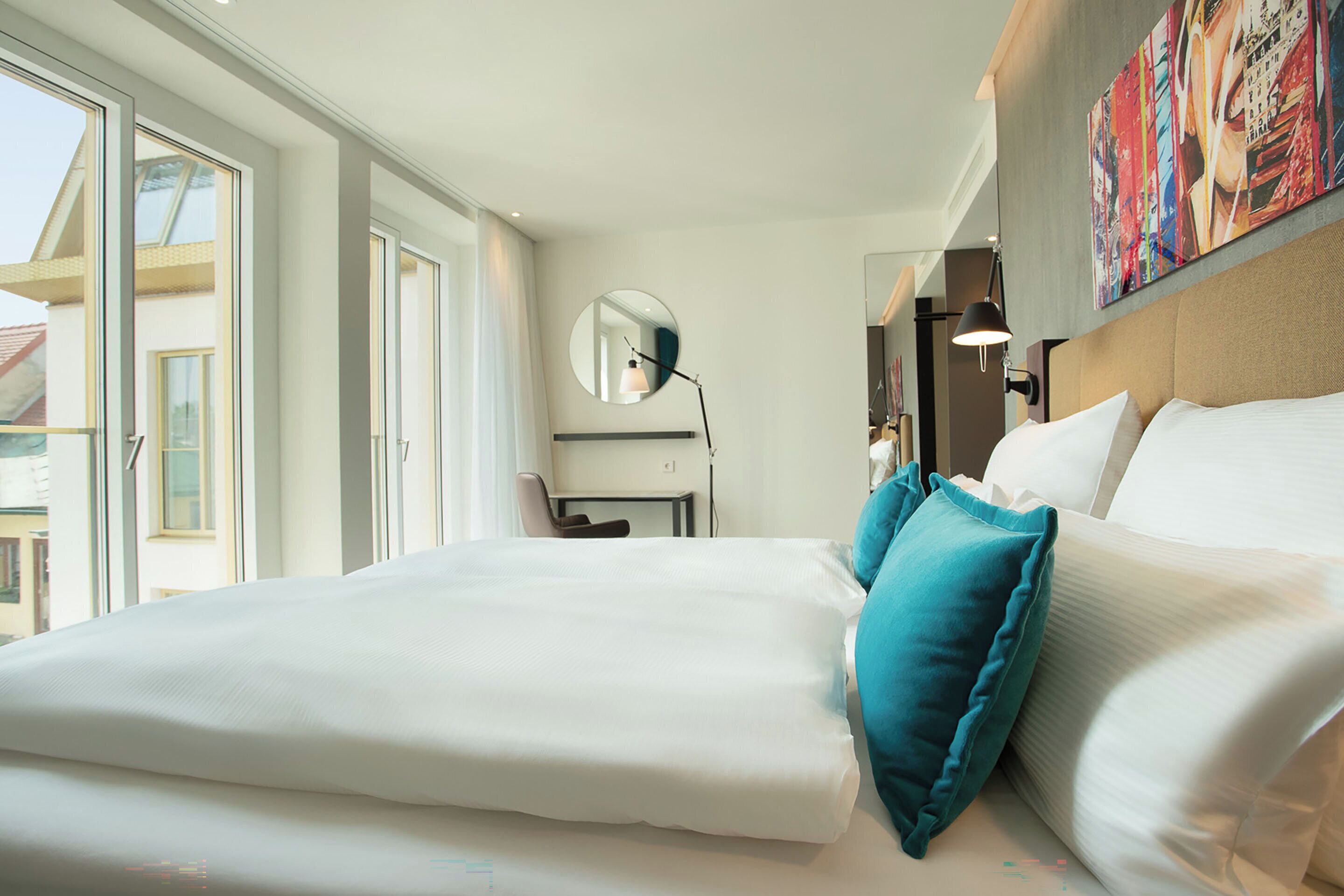 Hotelkamer met een groot bed, een bureau, een stoel, een ronde spiegel en een schilderij aan de muur.