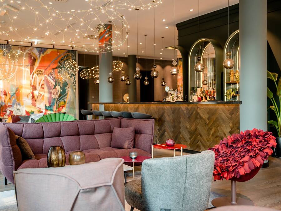 A modern interior with a plush seating area, a bar with a herringbone wood wall, and decorative lighting.