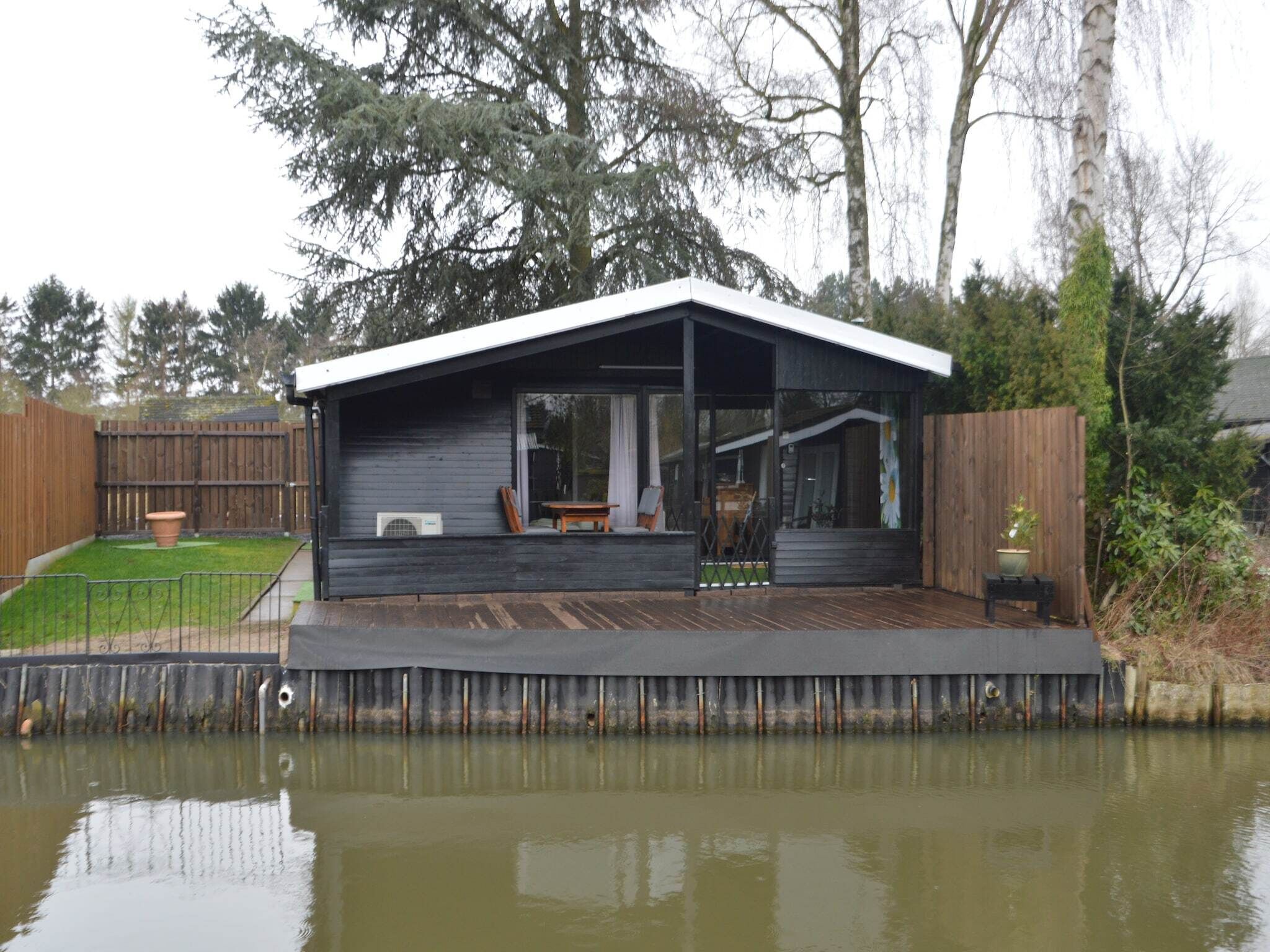 Une maison dotée d’un porche abrité, d’une petite terrasse et d’un étang en premier plan.