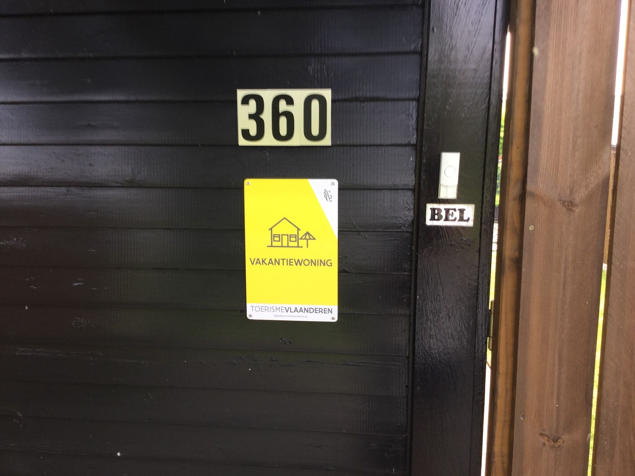 Une porte avec une enseigne indiquant « 360 » et « BEL », et une autre enseigne jaune en dessous indiquant « VAKANTIEWONING » et « TOERISMEVLAANDEREN ».