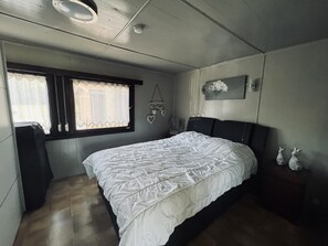 Et soveværelse med en stor seng, et vindue med gardiner, et natbord med pyngeting og et billede hængende på væggen.