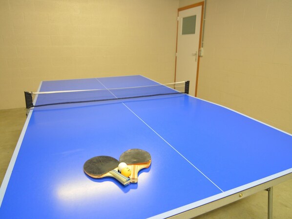 A ping pong table with two paddles and a ball in a room with beige walls and a door.