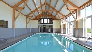 Una piscina interior con vigas de madera, paredes de azulejos y ventanas amplias.
