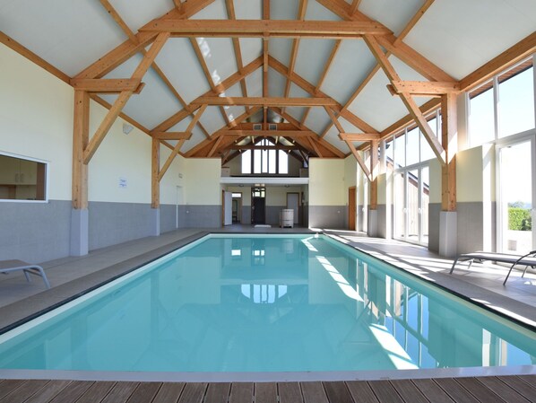 An indoor swimming pool with wooden beams, tiled walls, and large windows.