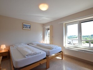 A room with two beds, a window with a view, a lamp, and a ceiling light.
