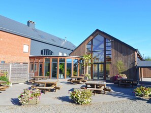 A building with a brick facade, large windows, and wooden picnic tables in the courtyard.