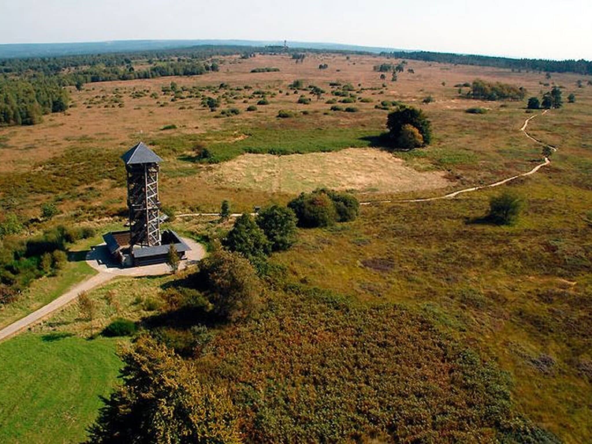 A tower structure with a viewing platform, surrounded by open fields and sparse vegetation.
