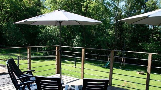 Een terras buiten met een tafel en stoelen, omgeven door een houten balustrade, met uitzicht op een gazon.