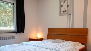 Een slaapkamer met een bed, nachtkastje, raam met gordijnen en een wandlamp.