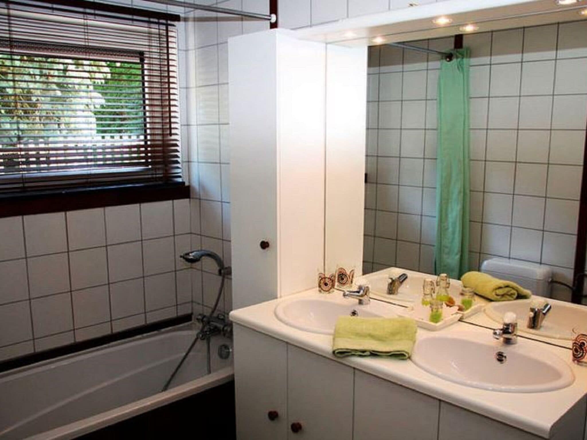 A bathroom with two sinks, a bathtub, and a window with blinds.