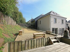 A wooden deck with benches, a fenced garden area, and a building with a sloped roof.