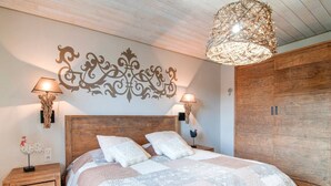 Une chambre à coucher avec une tête de lit en bois, deux tables de chevet avec des lampes, un grand lit recouvert d’une courtepointe et un élément décoratif mural au-dessus du lit.