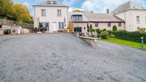 Un grand bâtiment à deux étages, avec une allée de gravier menant à un espace extérieur abrité, aménagé pour s’asseoir.