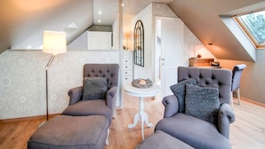 Une chambre mansardée chaleureuse, avec un plafond en pente, deux fauteuils, une petite table et une fenêtre offrant une belle vue.