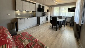 Eine kompakte Küche mit modernen Geräten, ein Essbereich mit Tisch und Stühlen und ein gemütliches Bett mit einem gemusterten Überwurf.