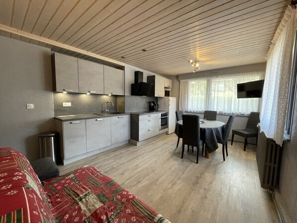 Een compacte keuken met moderne apparatuur, een eethoek met een tafel en stoelen, en een gezellig bed met een gestreept deken.