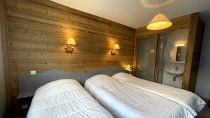 Ein Hotelzimmer mit zwei Einzelbetten, Holzvertäfelung, einer Holztür, einem Spiegel, einem Waschbecken und zwei Wandleuchten.