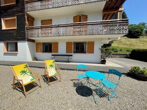 Een gebouw met twee verdiepingen, een balkon, een terras met stoelen en een tafel, en een bank.