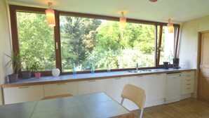 Une cuisine dotée d’une grande fenêtre, de meubles de rangement en bois, d’une table à manger et d’une chaise.