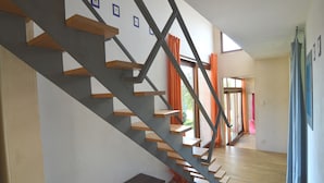 Un escalier moderne avec des marches en bois et des rampes en métal, menant à une pièce dotée de grandes fenêtres et de rideaux orange.
