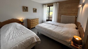 A bedroom with two beds, a wooden dresser, and a window with curtains. - GROTTE AUX FÉES A – Ski-in/ski-out apartment – ​​Wi-Fi – Parking (La Clusaz)