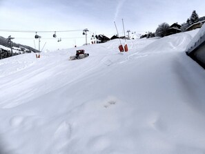 Ein verschneiter Ski-Hang mit einer Seilbahn und Gebäuden im Hintergrund.