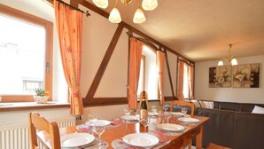 A dining area with a wooden table set for six, flanked by chairs, with a sofa and a bench in the background. - Holiday home in Butgenbach near the Lake (Bütgenbach)