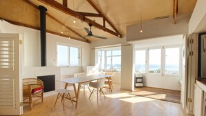 A spacious room with a large wooden table, a ceiling fan, and large windows offering a view of the ocean. - Spacious, Light and Bright on the Beachfront!!! (Cape Town)