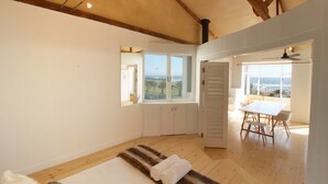 A bedroom with a large window, a bed, a wooden floor, and a view of the ocean. - Spacious, Light and Bright on the Beachfront!!! (Cape Town)