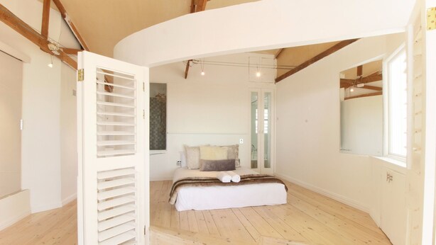 A bedroom with a curved ceiling, wooden flooring, a bed with white bedding, and a large mirror on the wall. - Spacious, Light and Bright on the Beachfront!!! (Cape Town)