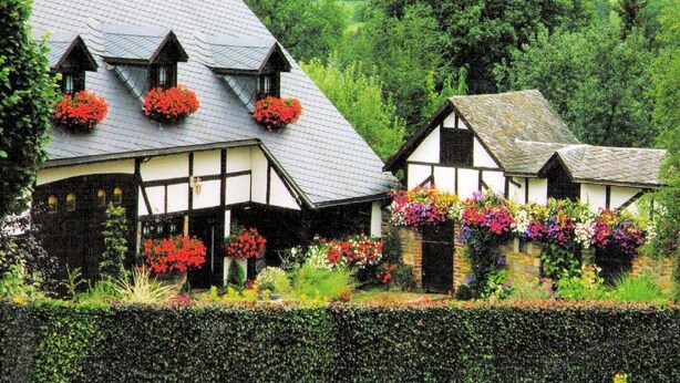Ein traditionelles Fachwerkhäuschen mit zahlreichen Blumenkästen am Dach und einem gepflegten Garten.