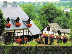 Una casa tradicional de entramado de madera con numerosos jardineros en el tejado y un jardín bien cuidado.