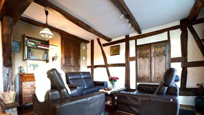 Ein traditionell eingerichteter Raum mit freiliegenden Holzbalken, Ledersofas, einem Holzschrank und einem kleinen Tisch mit Blumen.'