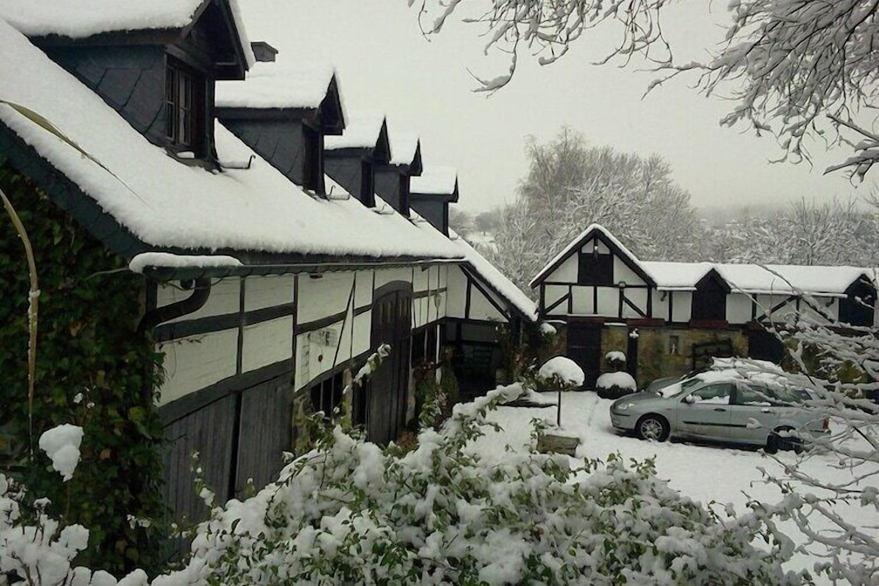 A traditional half-timbered building with a snow-covered roof and adjacent parking area.