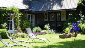 Ein Garten mit Liegestühlen, ein Steinhaus mit Ziegeldach und verschiedenen Pflanzen und Blumen.